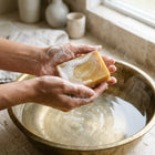 Nivam Turmeric & Coconut Milk soap bar lathering in hands over a brass basin